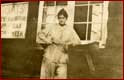 Myrtle Philip standing in front of Rainbow Lodge beside boat rental sing, c. 1914.