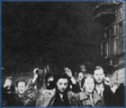 Jews are marched through the streets of the Warsaw ghetto as it burns.