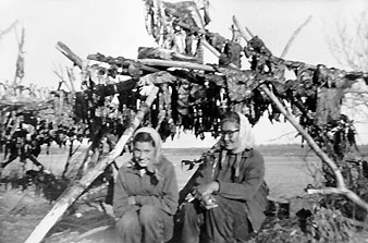 picture of Alice and Clara Frost sitting in front of a  rack of drying caribou meat
