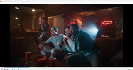 A still representation of video where three men are sitting on a couch and cheering, presumably watching a sports game on tv. Another man is sitting on a barstool also watching the tv, but not cheering.