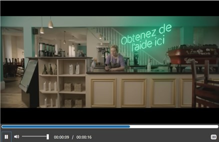 Une représentation fixe d'une vidéo où l'on voit un barista utiliser leur téléphone cellulaire en s'appuyant sur le comptoir du café. Le texte dit : 'Obtenez de l'aide ici'.