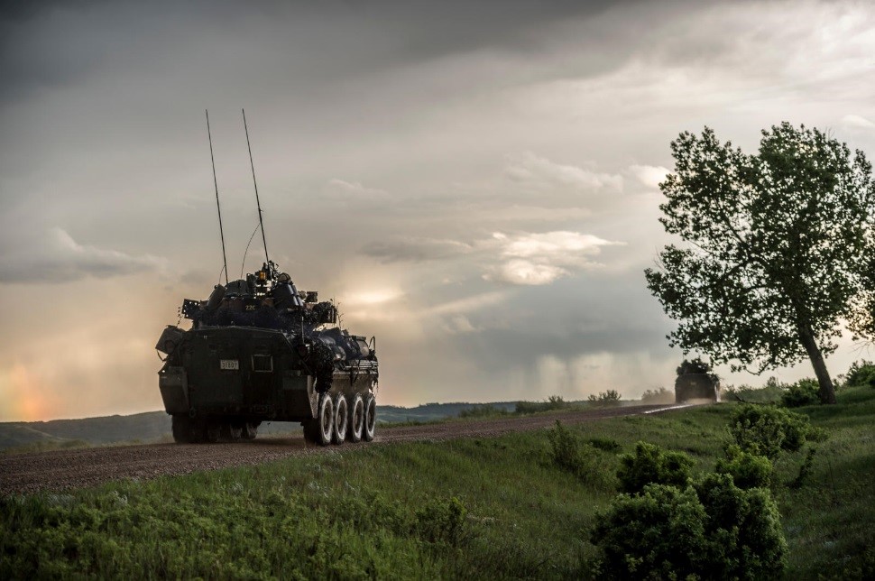 Two armoured vehicles travelling down a rural dirt road.