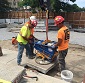 Three construction workers using a tool to move paving stones.