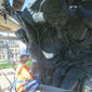 A woman in a hard hat and personal protective equipment works on a bronze statue.