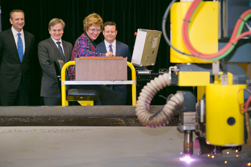 A woman operating machinery, while three men stand behind.