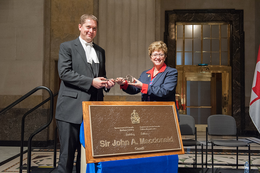 A woman handing over a large key to a man.