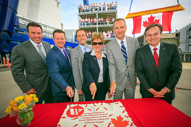 A group of men and a woman cutting a cake.