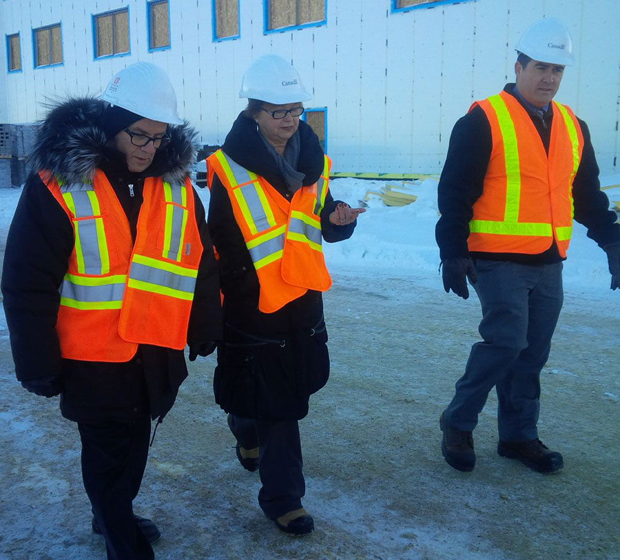 Trois personnes portant casques et vestes de sécurité marchent près d'un immeuble en construction.