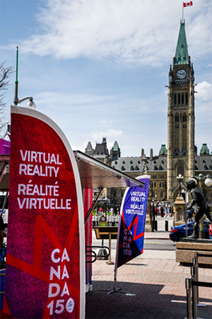 Des bannières drapeaux se trouvent aux deux extrémités du kiosque de réalité virtuelle. Il y a la tour de la Paix à l’arrière-plan.