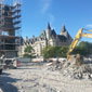 A view of a construction site with a monument covered in scaffolding in the background and a backhoe moving broken concrete in the foreground.