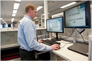 Employee working from a height-adjustable workstation with two computer monitors, Ottawa, ON