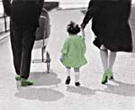 Black and white photograph of a child wearing a green dress and her parents wearing green shoes taking a stroll